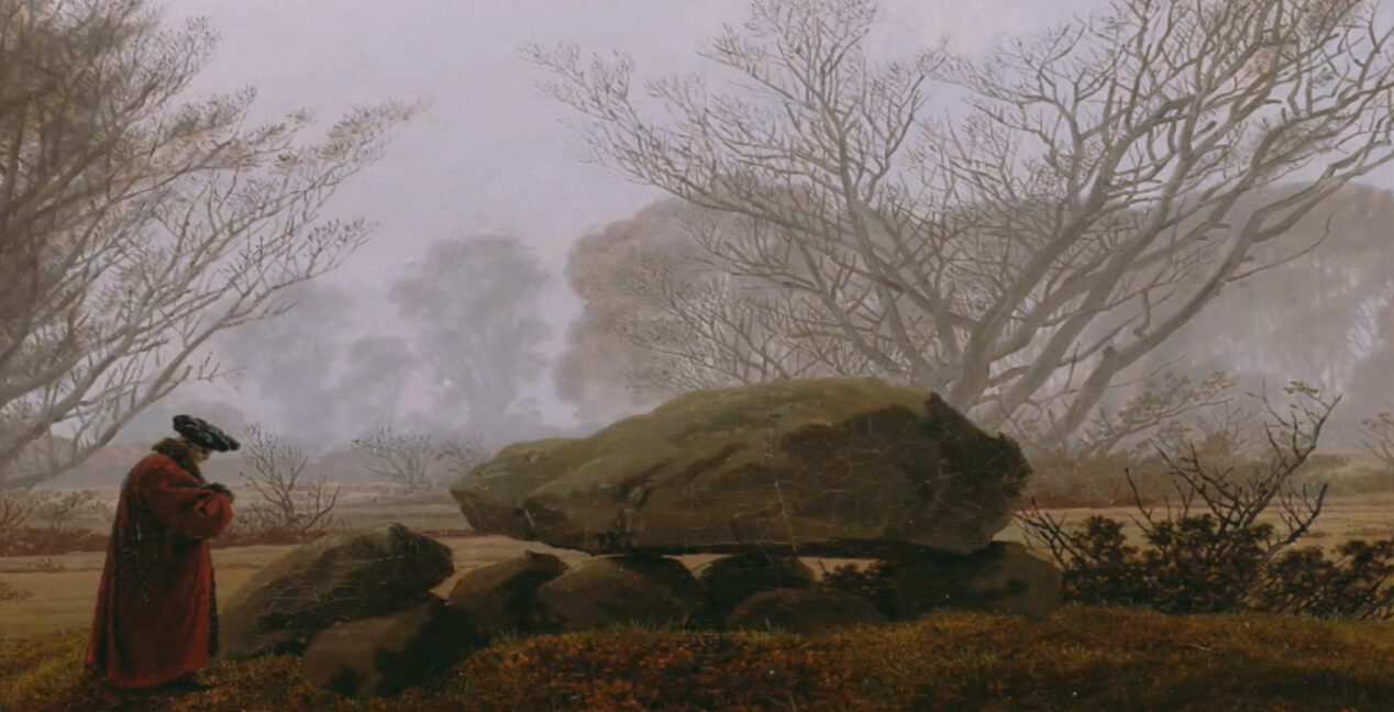 A lone figure in a red cloak stands beside a large boulder in a misty, leafless landscape at dusk.