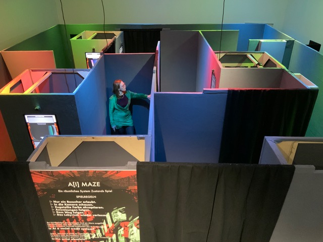 A person stands in a colorful indoor maze of tall partition walls with a sign reading A/I Maze in front.
