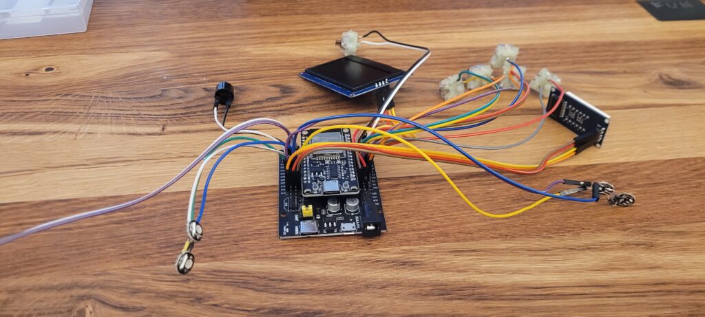 An ESP32 board, wires, a small display, and loose components are spread on a wooden tabletop.