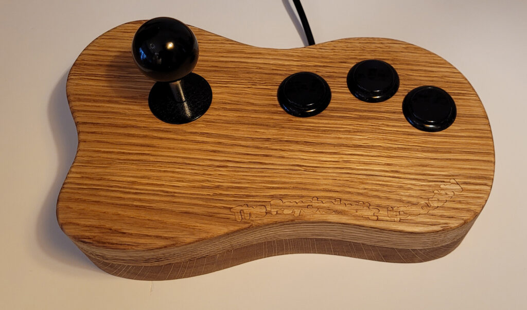 Wooden arcade controller with a black joystick and three black buttons on a curved carved body