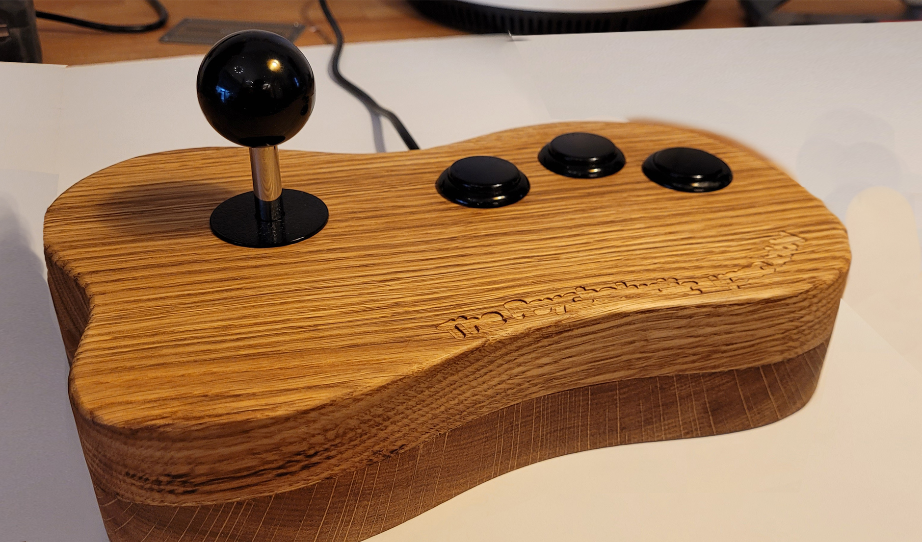 Wooden game controller body with a black joystick and three black buttons on top.