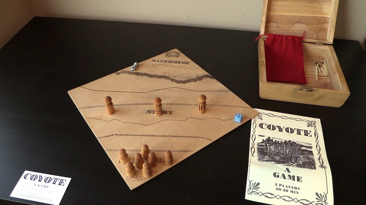A tabletop board game setup with a wooden board, small figurines, cards, and an open box.