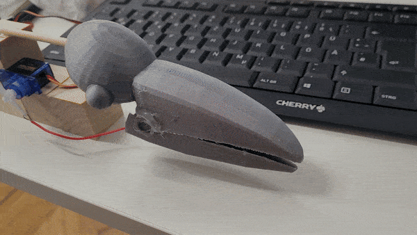 3D-printed raven head on a desk beside a keyboard, with servo wires attached.