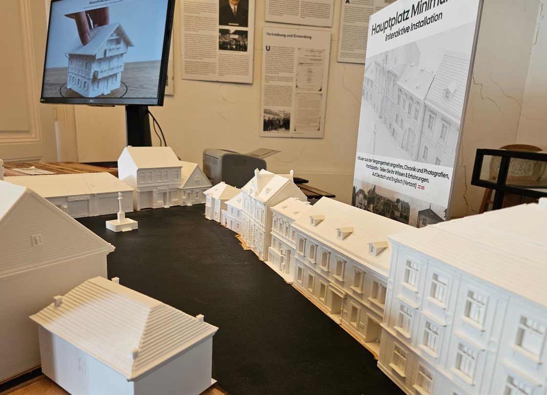 The white 3D-printed houses of the Hauptplatz model on a black base, the display and exhibition panels behind.