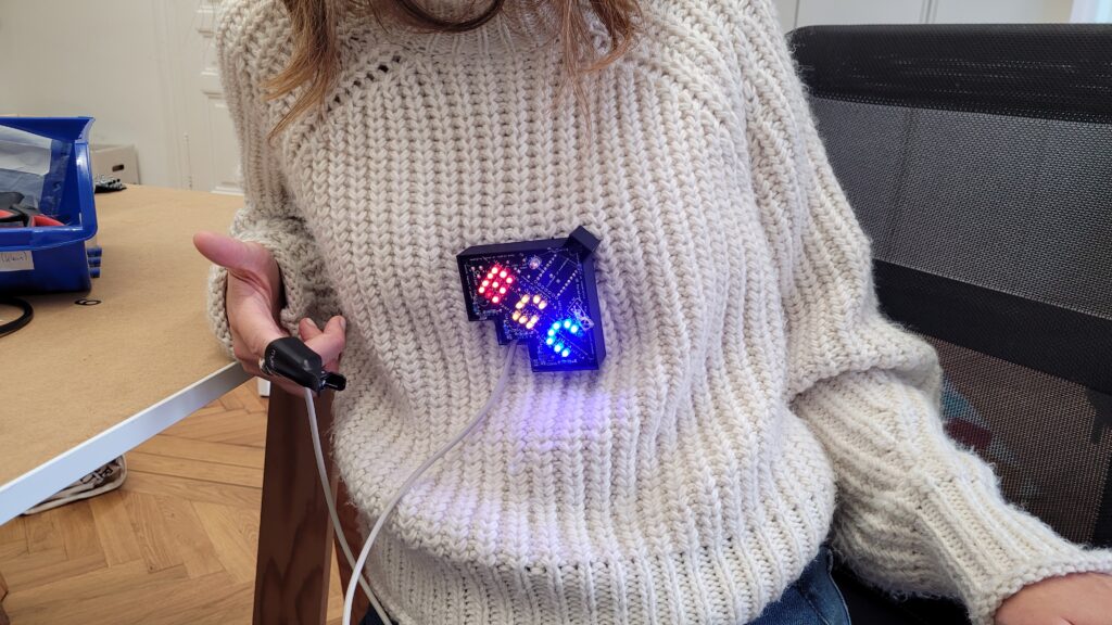 Person in a cream sweater holds a lit custom circuit board with wires attached.