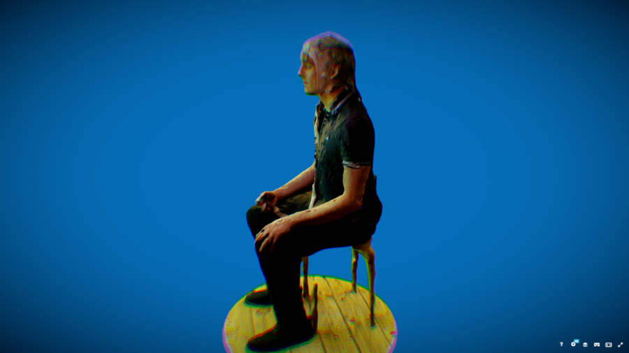 A man sits on a chair on a round wooden platform against a solid blue background.