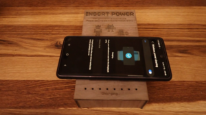 A smartphone rests on a laser-cut wooden charging base with a display and small LEDs on top.