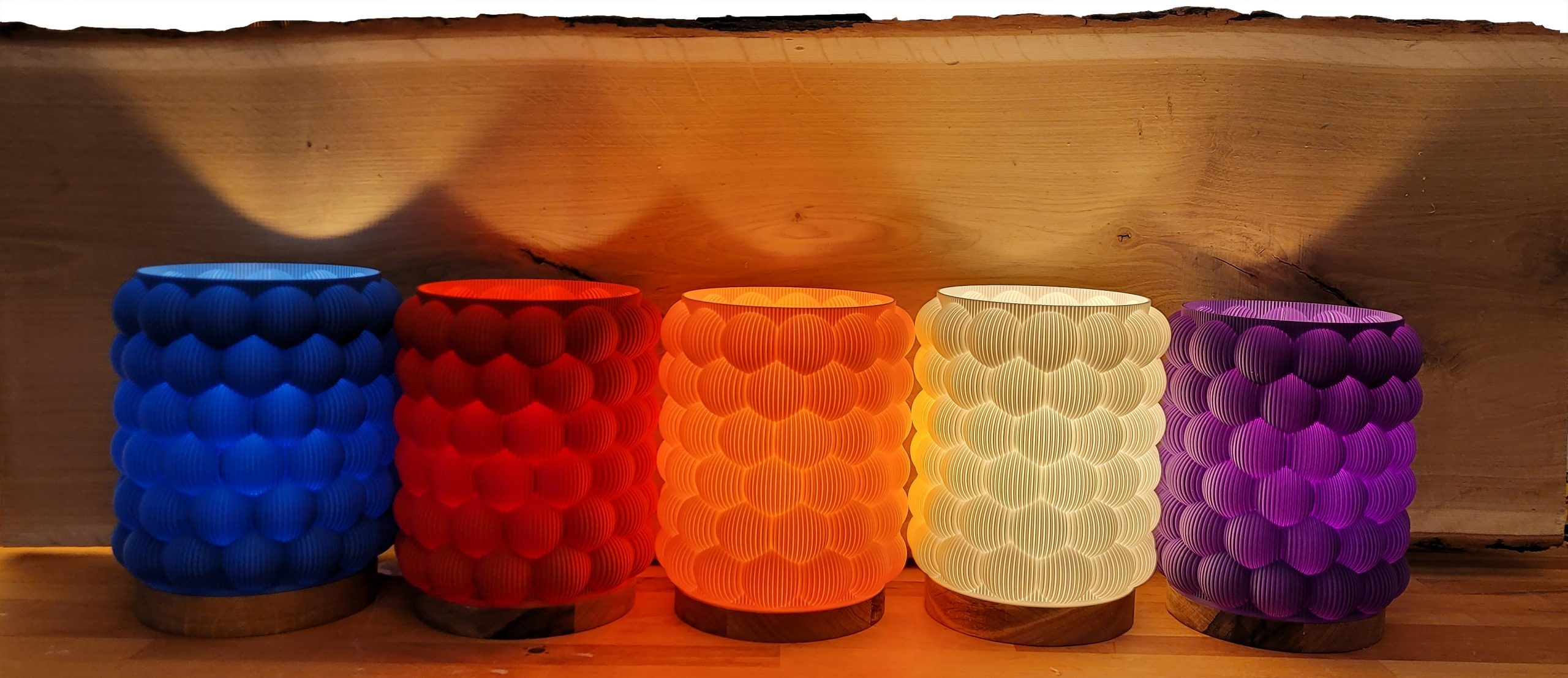 Five scaled lamps in blue, red, orange, white and violet glow in a row on a wooden shelf